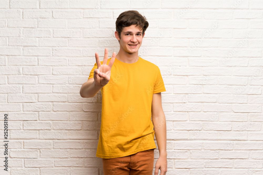 Teenager man over white brick wall happy and counting three with fingers Teenager man over white brick wall happy and counting three with fingers
