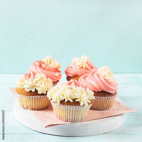 Fresh cupcakes with whipped cream and cream are served on a plate on a soft blue background close-up. Copy space.