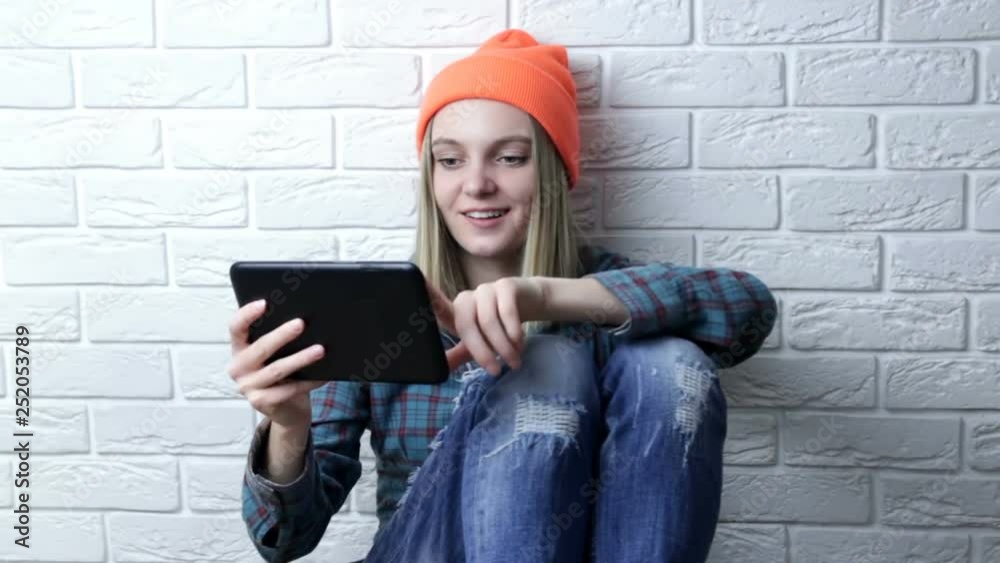 Fashion hipster stylish young woman in orange hat using tablet pc over white brick wall Fashion hipster stylish young woman in orange hat using tablet pc over white brick wall