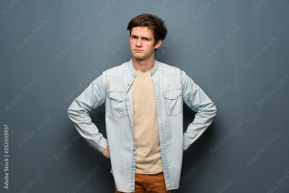Teenager man with jean jacket over grey wall angry Teenager man with jean jacket over grey wall angry