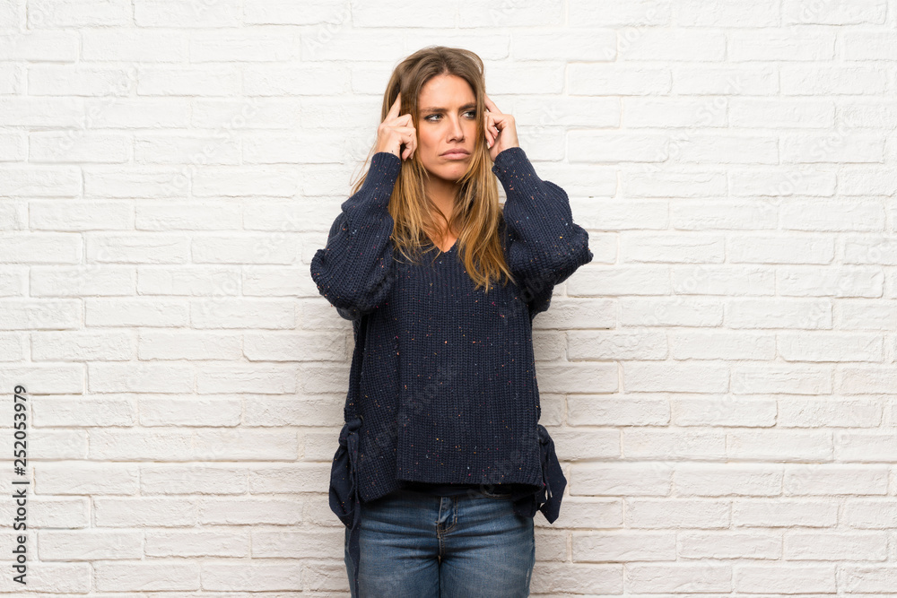 Blonde woman over brick wall having doubts while scratching head Blonde woman over brick wall having doubts while scratching head