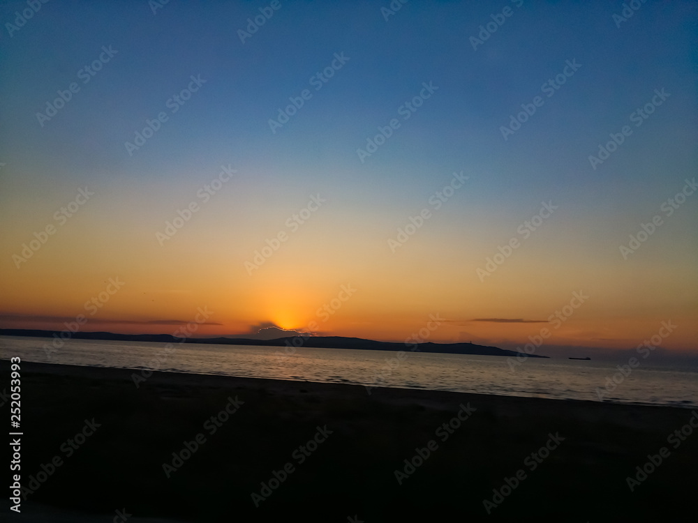 Sunset sky over the quiet sea. On the horizon a cape and sailing ship