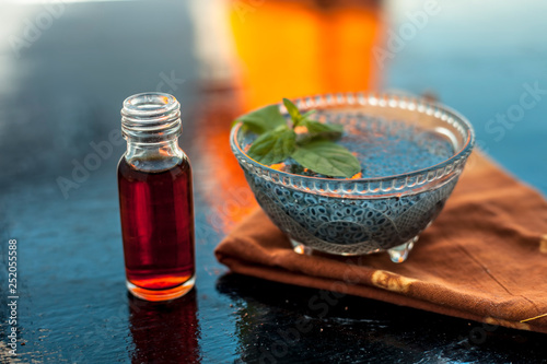 Glass bowl full of soaked sabja seeds or falooda seeds or sweet basil seeds with its extracted essence or essential oil in a transparent glass bottle on wooden surface. photo