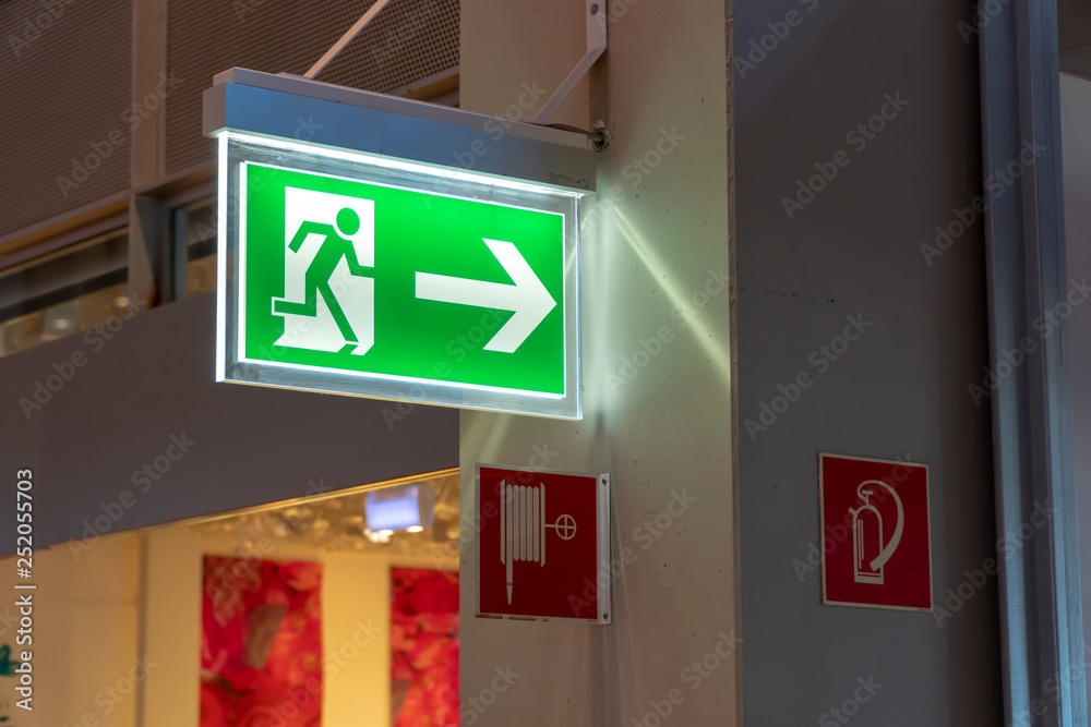 Lighted emergency green exit sign box in a German airport. Lighted emergency green exit sign box in a German airport.