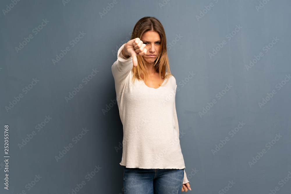 Fototapeta premium Blonde woman over grey background showing thumb down with negative expression