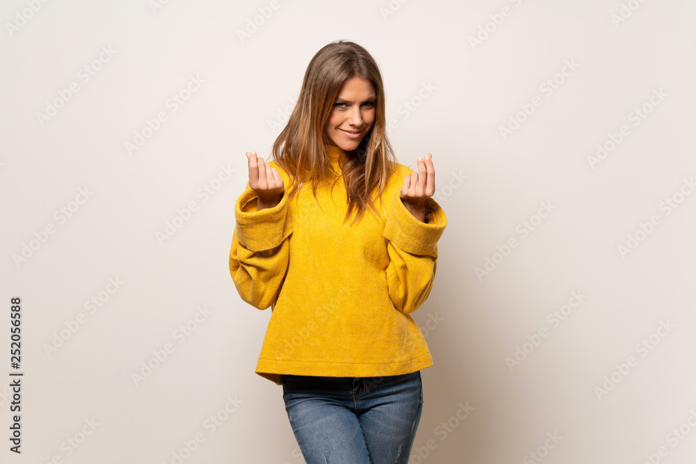 Woman with yellow sweater over isolated wall making money gesture