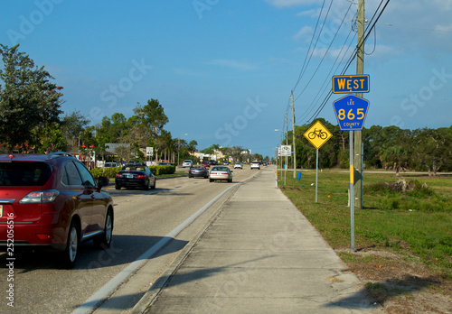 View from sidewalk of Bonita Beach Road during winter tourist season with traffic and road signs.
