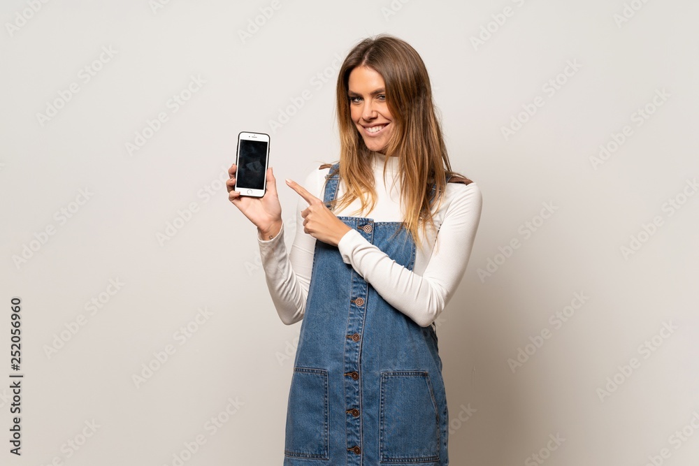 Beautiful woman over isolated white wall happy and pointing the mobile Beautiful woman over isolated white wall happy and pointing the mobile
