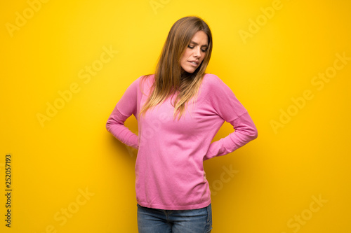 Woman with pink sweater over yellow wall suffering from backache for having made an effort