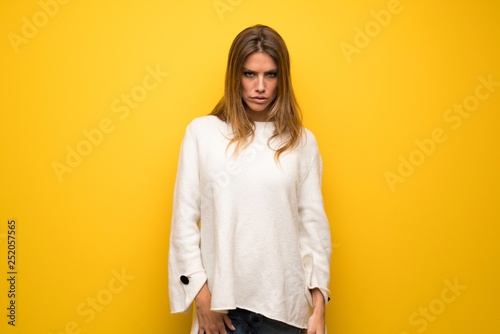 Blonde woman over yellow wall with sad and depressed expression