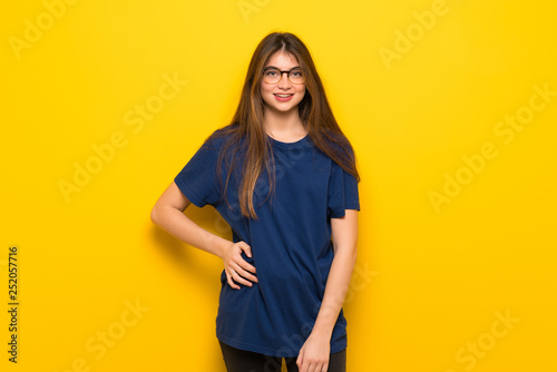 Young woman with glasses over yellow wall posing and laughing looking to the front © luismolinero