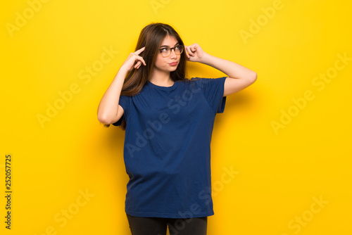Young woman with glasses over yellow wall having doubts and thinking