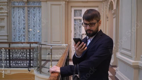 A young handsome businessman with glasses and beard hears a call and answers by mobile phone. Talking on the phone and smiling photo