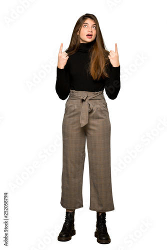 Full-length shot of Pretty girl surprised and pointing up on isolated white background