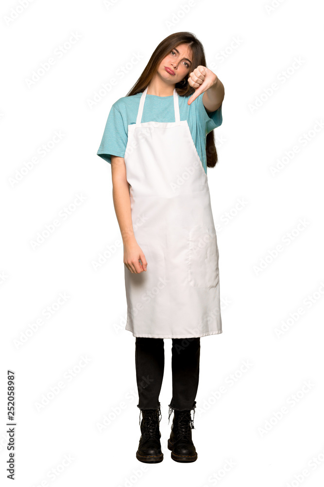Full-length shot of Girl with apron showing thumb down sign with negative expression on isolated white background Full-length shot of Girl with apron showing thumb down sign with negative expression on isolated white background
