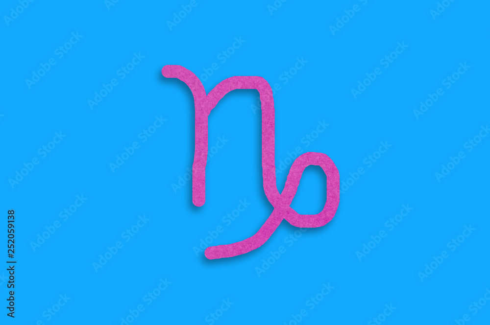 Symbol of astrological sign capricorn cut out of purple paper in center on blue table. Top view. Horoscope concept Symbol of astrological sign capricorn cut out of purple paper in center on blue table. Top view. Horoscope concept