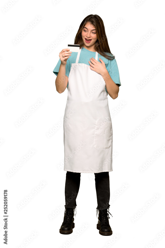 Full-length shot of Girl with apron holding a credit card and surprised on isolated white background Full-length shot of Girl with apron holding a credit card and surprised on isolated white background