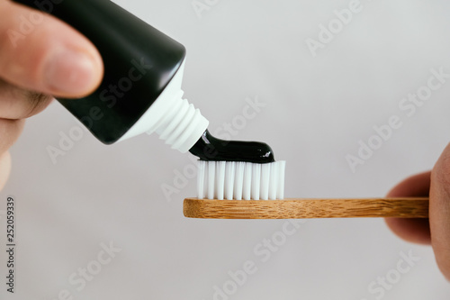 Canvas Print Close up of a male hands with a black toothpaste and a bamboo toothbrush