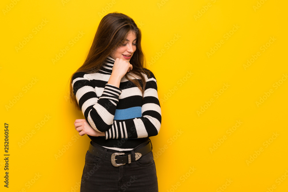 Young woman over yellow wall looking down with the hand on the chin Young woman over yellow wall looking down with the hand on the chin