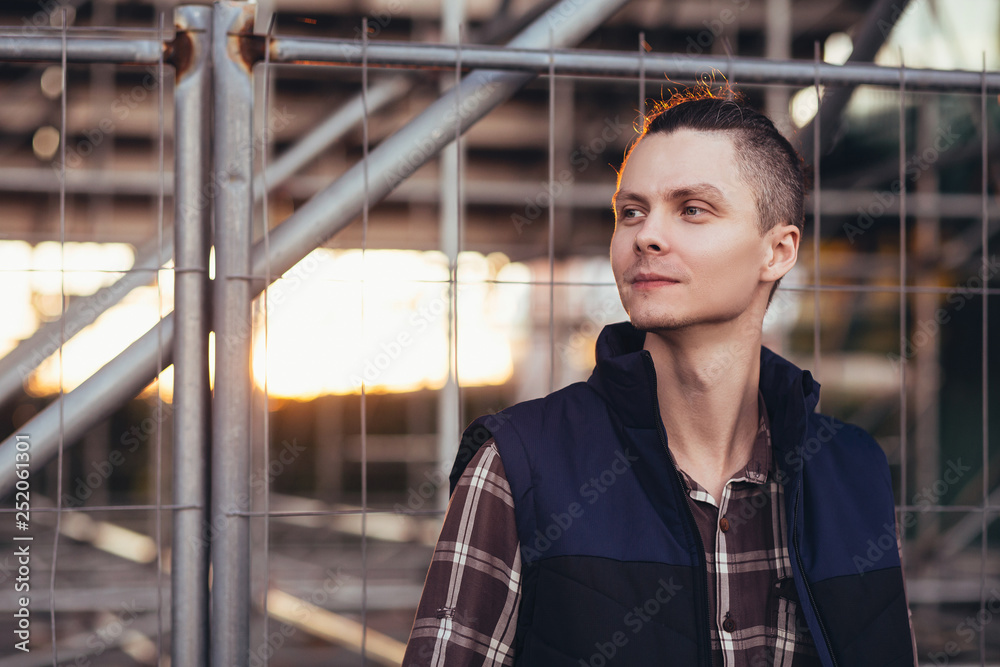 Fototapeta premium Cute young man traveler posing against a background of barred building with iron structures. The concept of tourist walks around the city