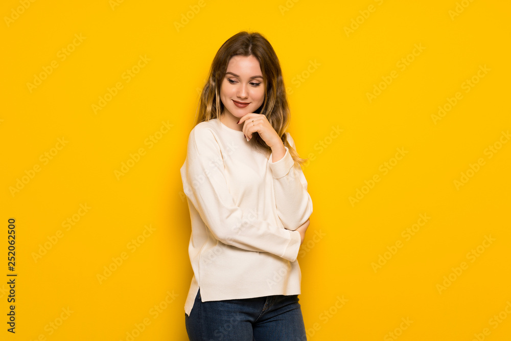 Fototapeta premium Teenager girl over yellow wall looking to the side with the hand on the chin