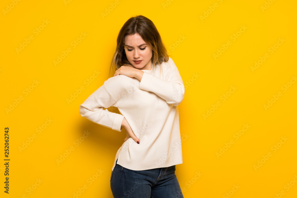 Teenager girl over yellow wall suffering from pain in shoulder for having made an effort Teenager girl over yellow wall suffering from pain in shoulder for having made an effort
