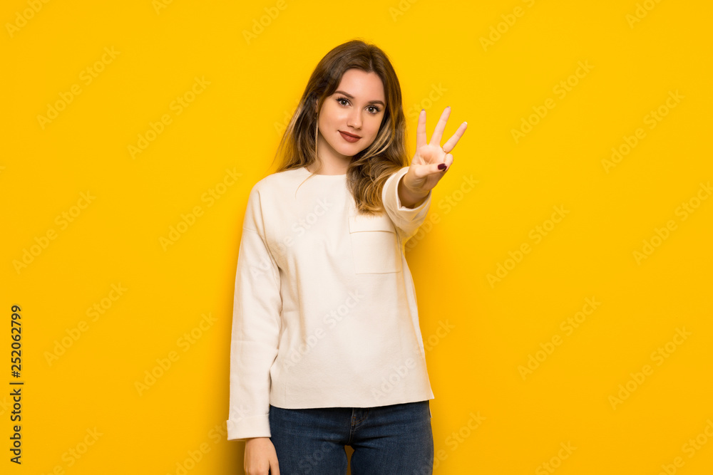 Teenager girl over yellow wall happy and counting three with fingers Teenager girl over yellow wall happy and counting three with fingers