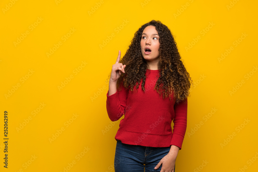 Teenager girl with red sweater over yellow wall thinking an idea pointing the finger up Teenager girl with red sweater over yellow wall thinking an idea pointing the finger up