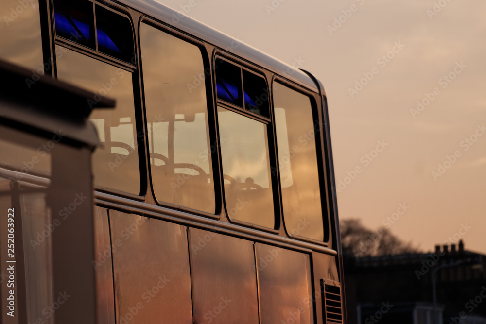 Side of a double decker bus with a sunset reflecting in the windows