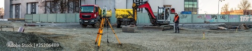 Panoramic view of surveyor engineer with equipment (theodolit or total positioning station) on the construction site of the road with construction machinery background