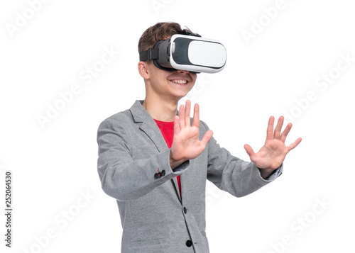 Happy Teen Boy wearing Virtual Reality Goggles watching movies or playing video games, isolated on white. Cheerful Teenager looking in VR glasses. Funny Child experiencing 3D gadget technology.