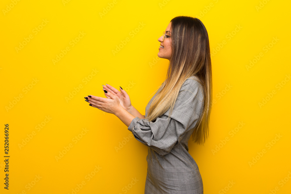Young woman with glasses over yellow wall applauding after presentation in a conference Young woman with glasses over yellow wall applauding after presentation in a conference