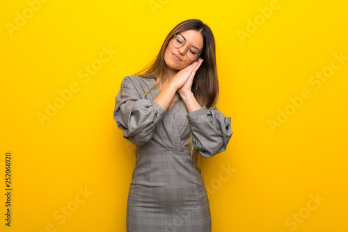 Young woman with glasses over yellow wall making sleep gesture in dorable expression