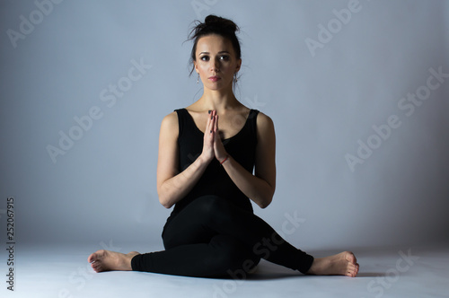 Beautiful young dark-haired girl in a black uniform and does yoga. Studio photos.