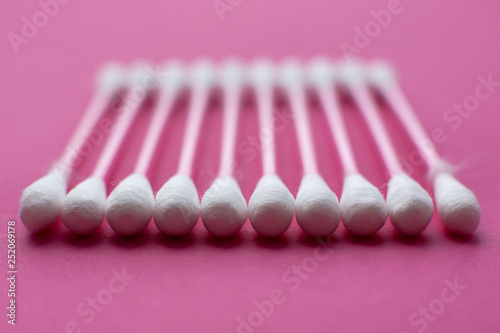 Closeup view from above on cotton buds laid in a horizontal line on pink background