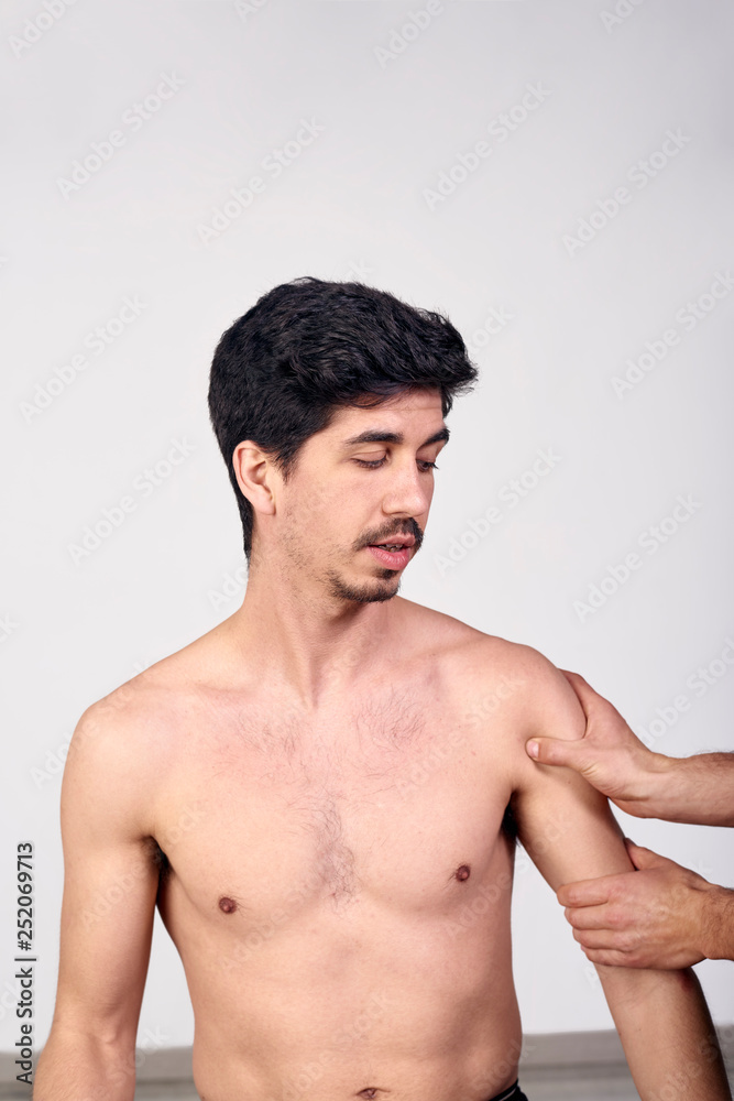 Fototapeta premium Young man having chiropractic shoulder adjustment. Physiotherapy, sports injury rehabilitation. Osteopathy, Alternative medicine, pain relief concept