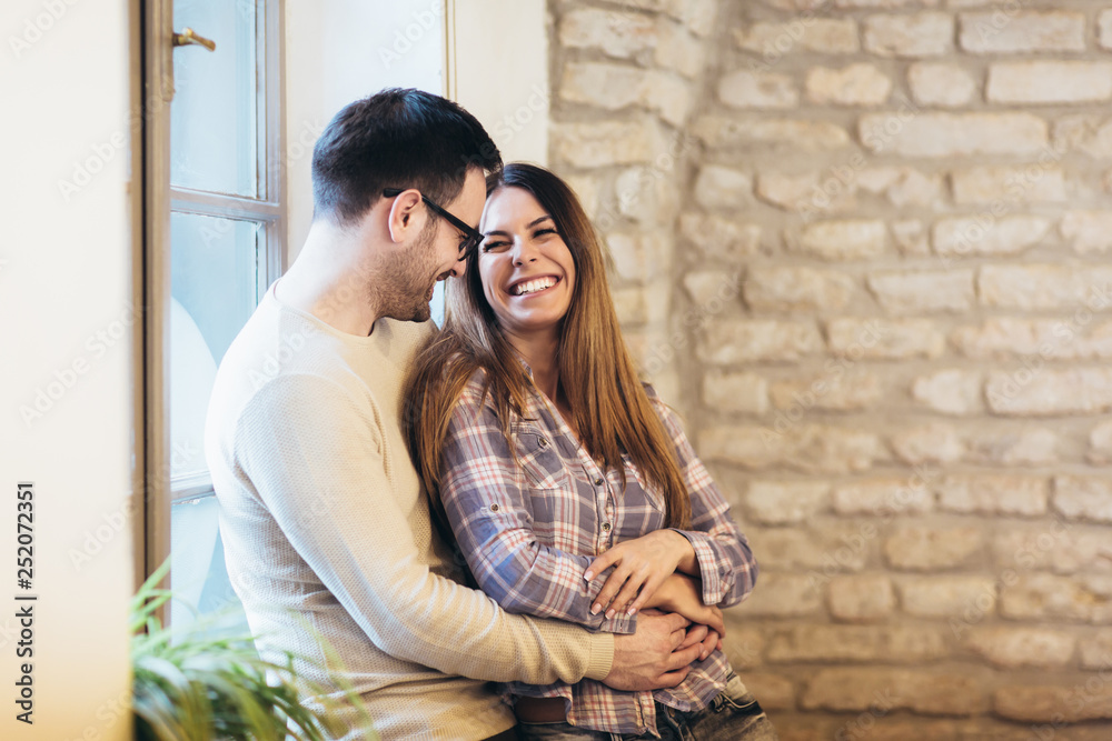 Portrait of a young couple hugging next to the window, brick wall background.