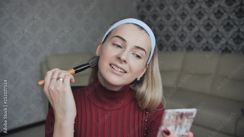 Blonde applying facial powder to herself with a brush. Blonde applying facial powder to herself with a brush.