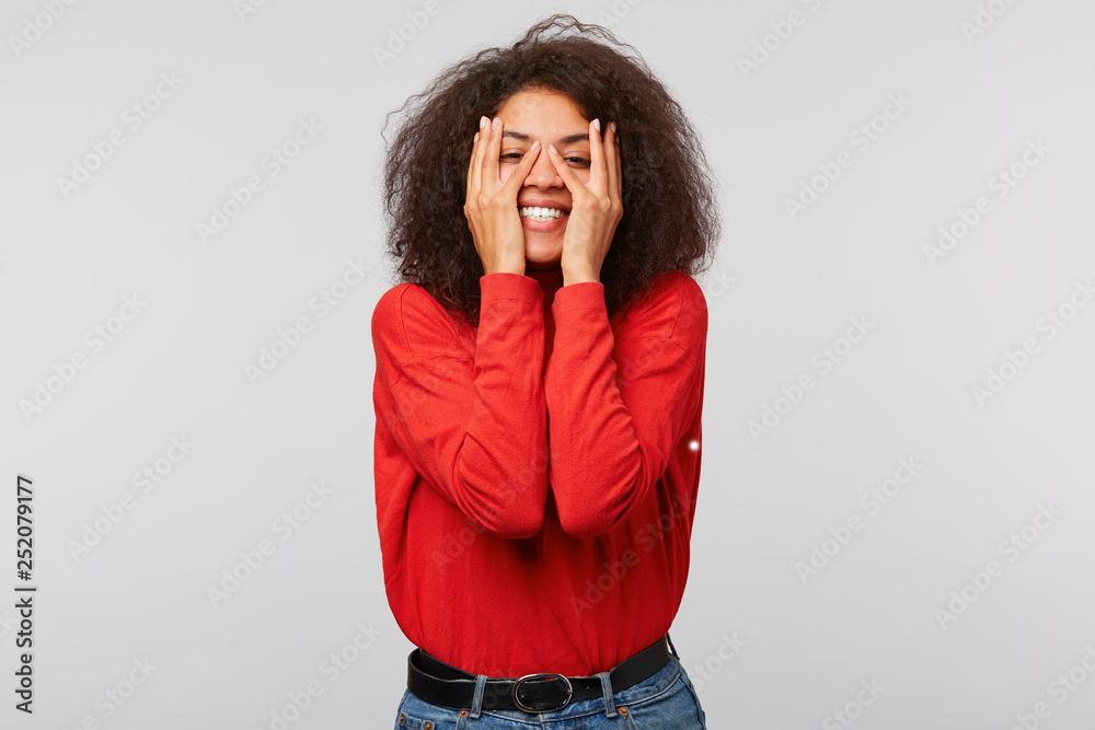 What life prepared next. Portrait of joyful attractive and carefree african female with trendy afro hairstyle, covering eyes with palms, peeking through the palms and smiling,over white wall What life prepared next. Portrait of joyful attractive and carefree african female with trendy afro hairstyle, covering eyes with palms, peeking through the palms and smiling,over white wall