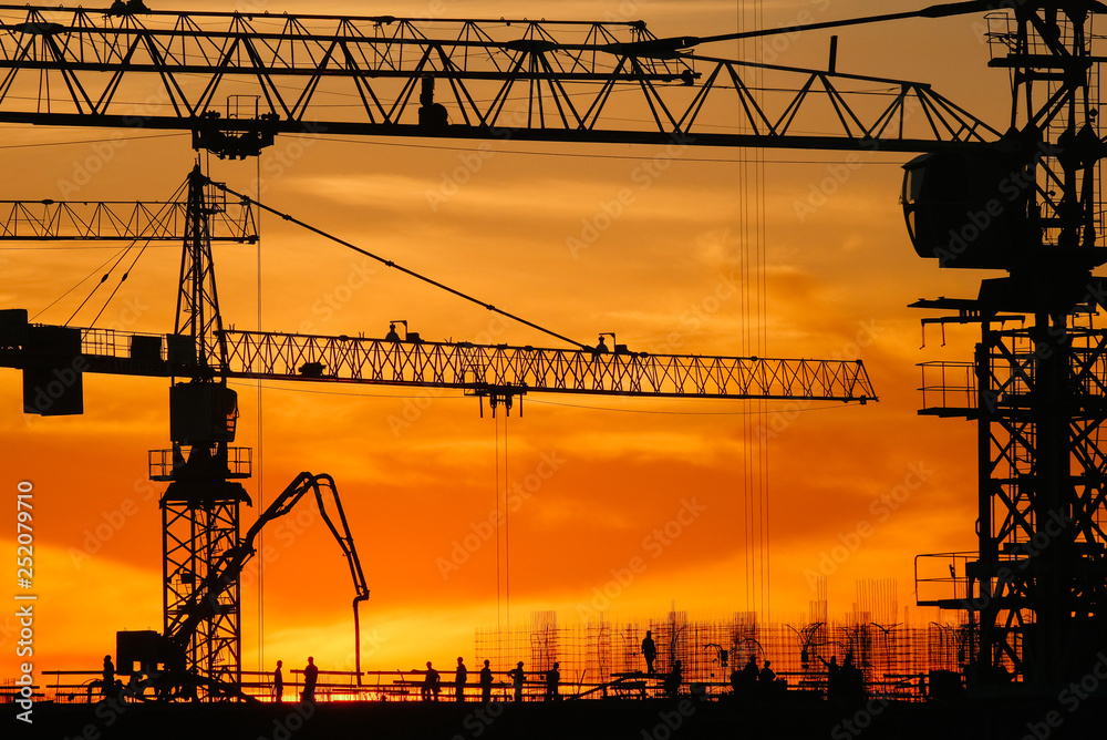 Cranes silhouettes in warm sunset lights with builders working on the roof 