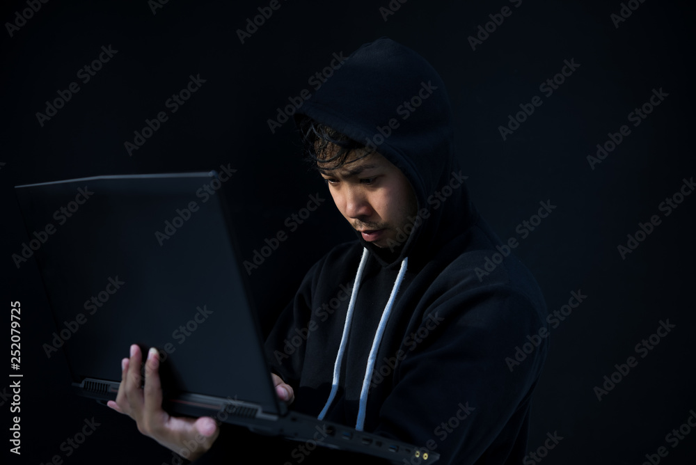 Asian hacker in black hood on black background,Hack password,hacking safety systems to steal information Asian hacker in black hood on black background,Hack password,hacking safety systems to steal information