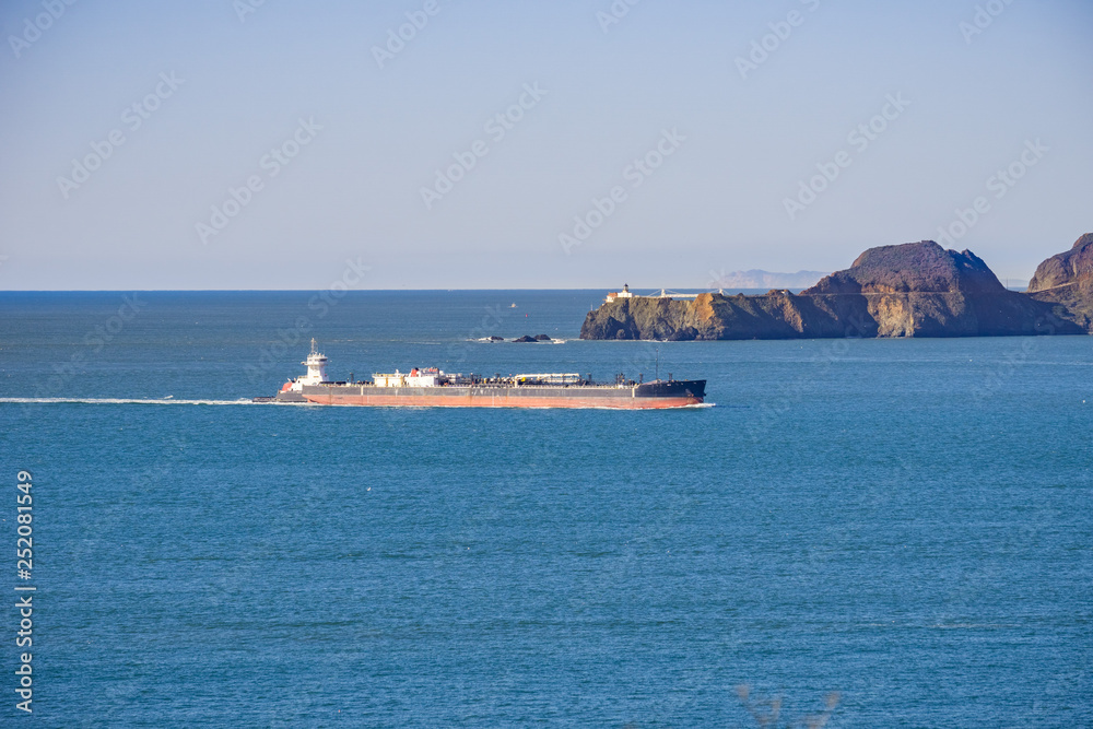 Cargo ship preparing to enter San Francisco bay; in the background Point Bonita Lighthouse, California