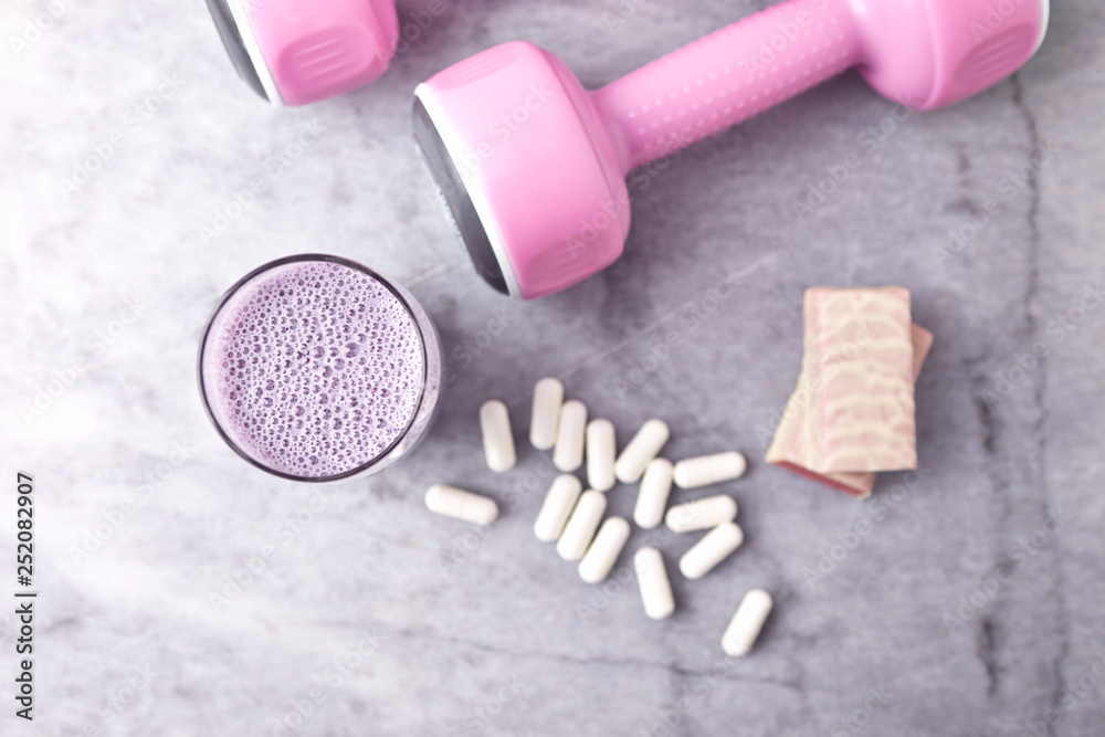 Glass of Protein Shake with milk and blueberries. BCAA capsules, Protein bar in two pieces and pink dumbbells in background. Concept for Sport nutrition. Stone background. Top view. Copy space. Glass of Protein Shake with milk and blueberries. BCAA capsules, Protein bar in two pieces and pink dumbbells in background. Concept for Sport nutrition. Stone background. Top view. Copy space.