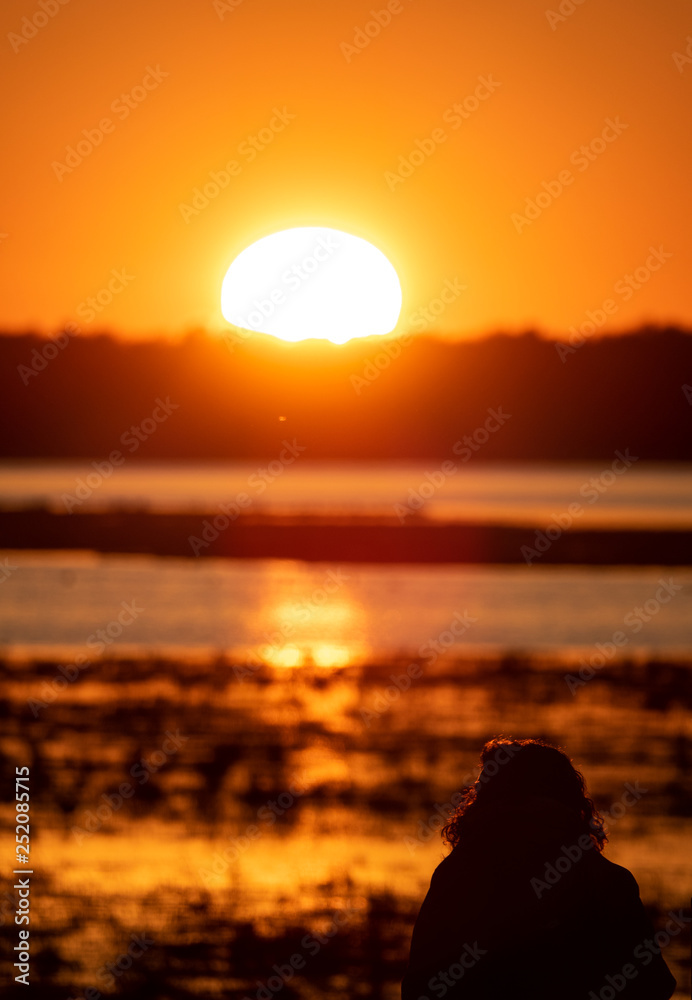 Woman silhouette observing sunrise over the lake