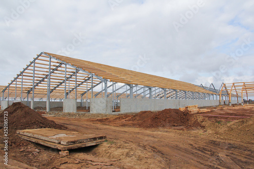 The frame of the roof of the new barn for cows. Construction of a new barn. Wooden beams on a metal frame. Construction of agricultural buildings.
