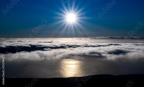 Bright sun reflection in the ocean over the clouds near coastline