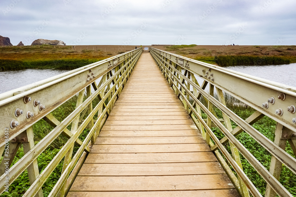 Obraz premium Wood and metal bridge crossing the Rodeo Lagoon towards Rodeo Beach, Headlands, Golden Gate Recreation Area, Marin County, California