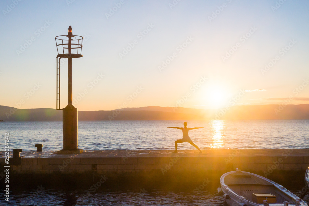 Woman doing yoga position and practicing meditation on a pier on the seaside. Yoga silhouette. Fitness and healthy lifestyle.