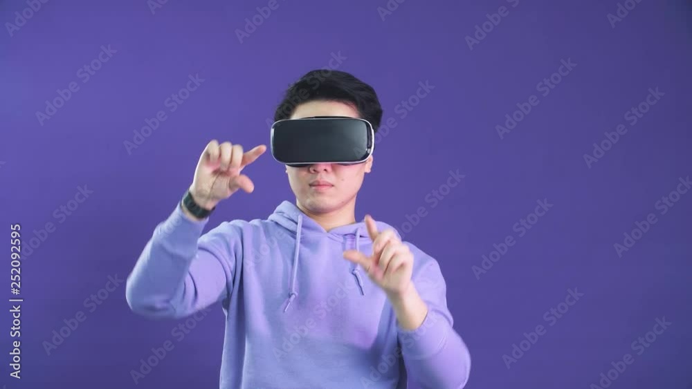 Young Asian man playing VR game in dark blue background. Chinese young hipster wearing VR headset. Young generation choose virtual reality concept. Young Asian man playing VR game in dark blue background. Chinese young hipster wearing VR headset. Young generation choose virtual reality concept.