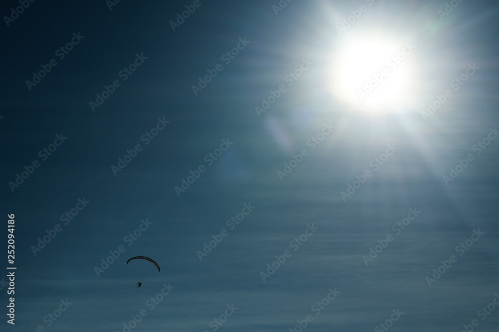 Silhouette of parachutist flying on parachute in the beautiful blue sky. Sun flares.